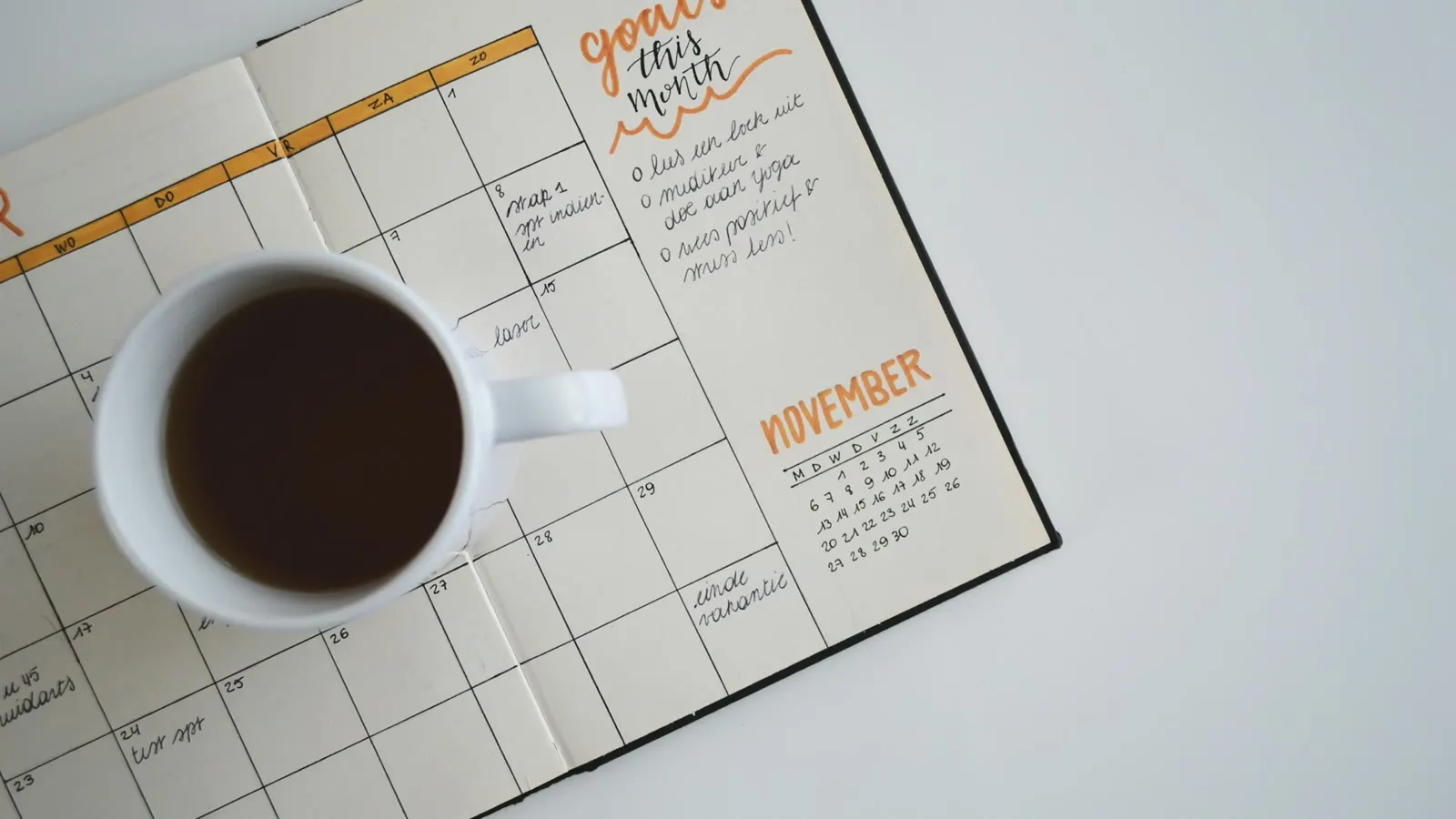 A weekly wall planner beside a cup of coffee