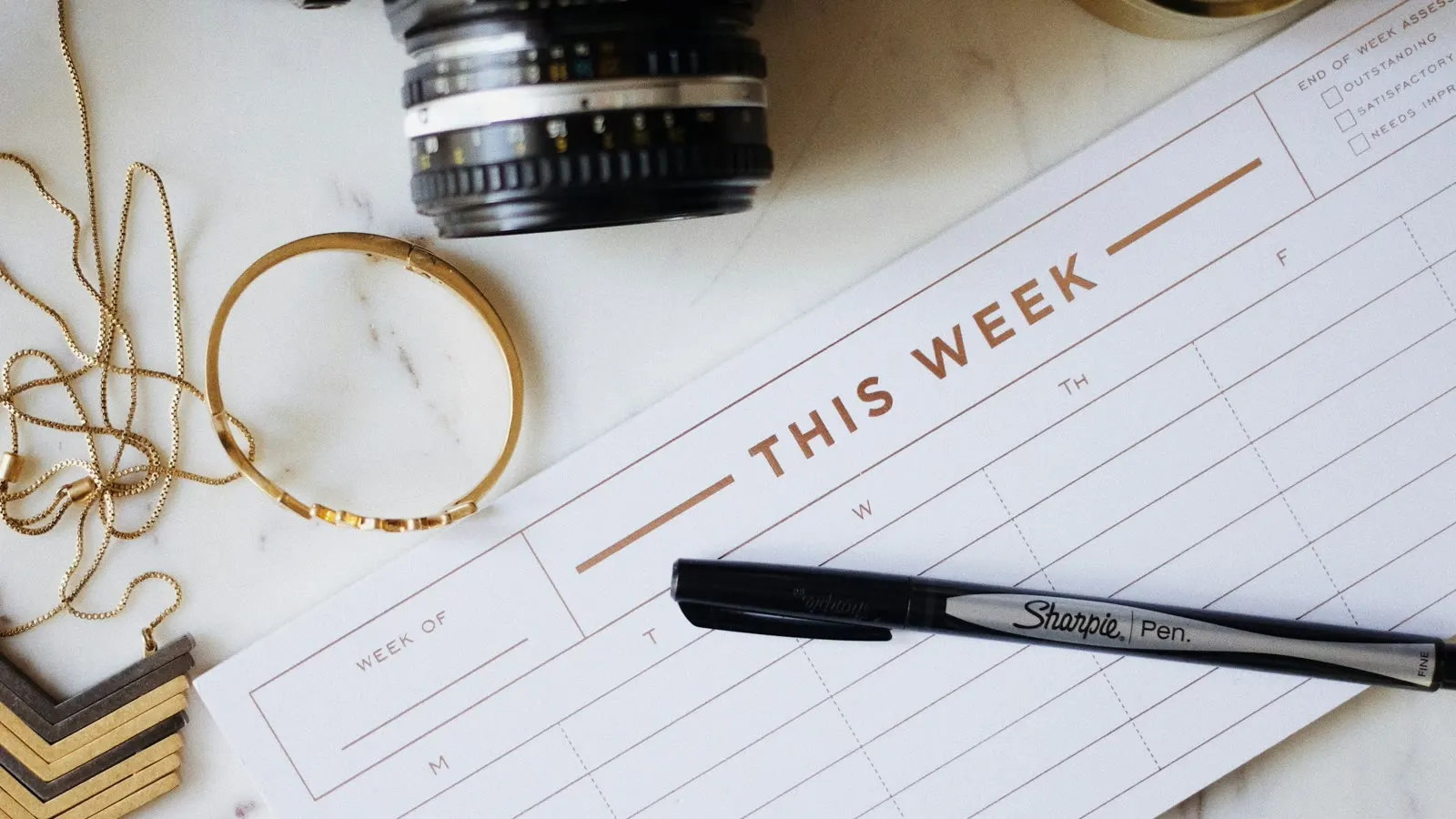 A weekly planning sheet beside a pen and camera